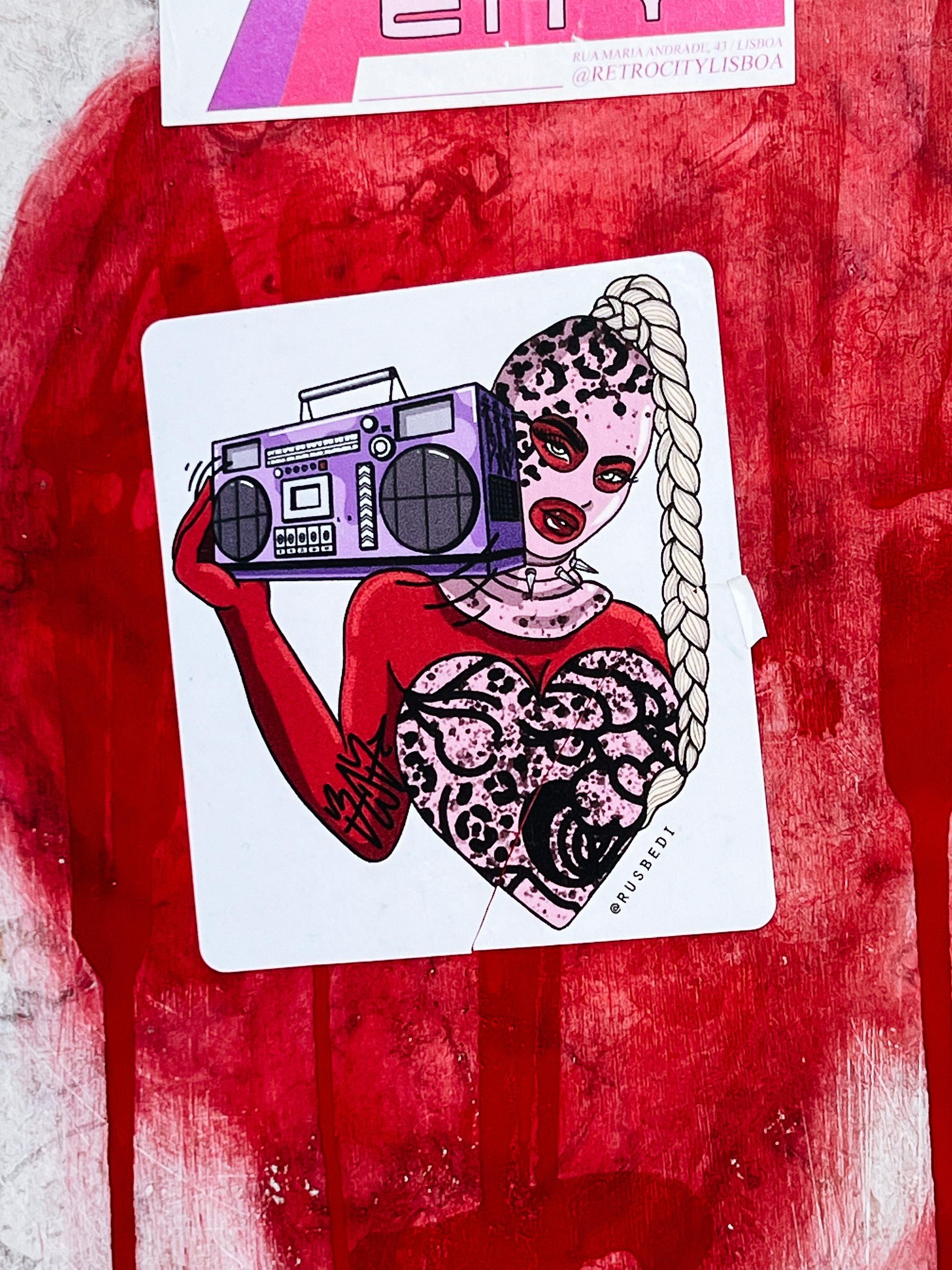 Sticker with a drawing, showing a girl with a pink balaclava, holding a boom box, wearing a red outfit with a heart. 
