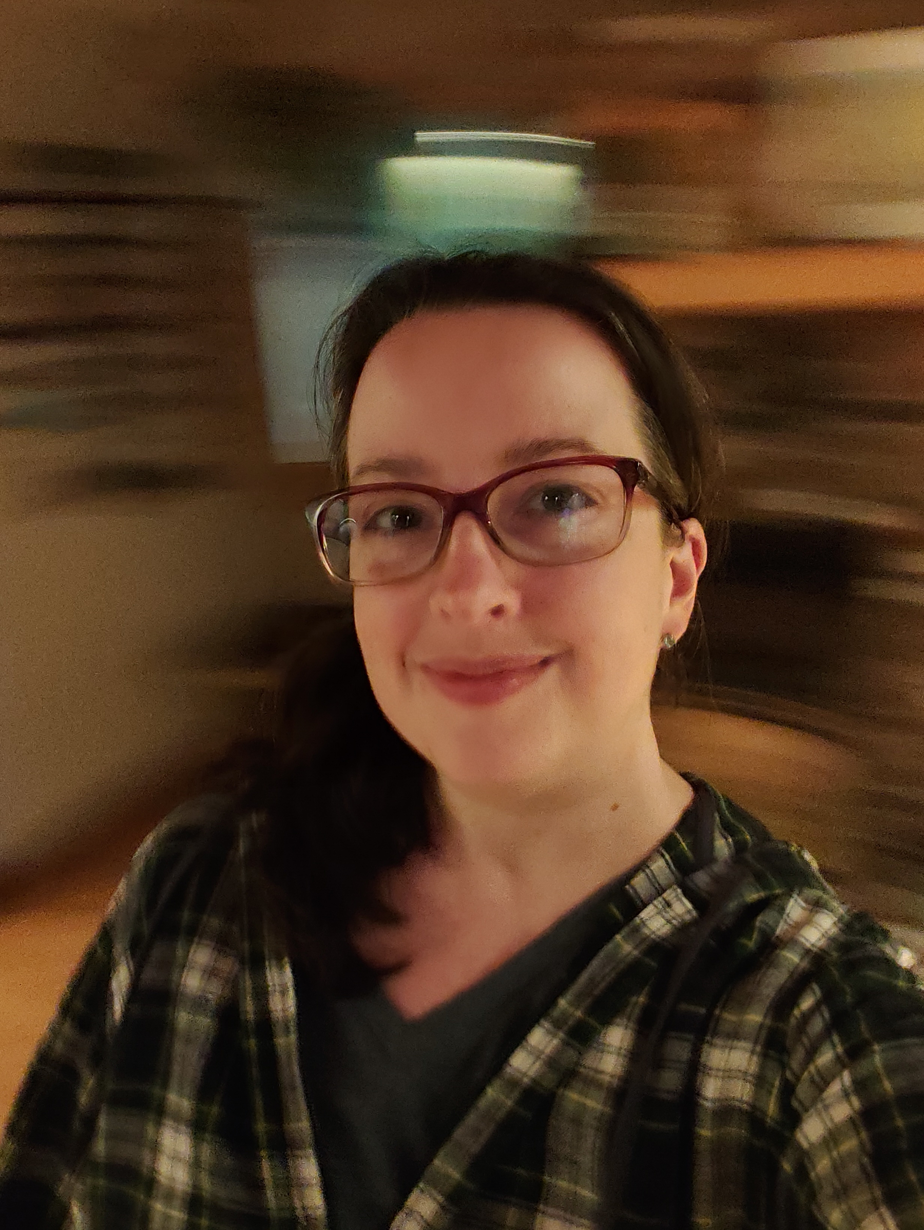A person wearing glasses and a plaid shirt smiles at the camera with a blurred background, giving a sense of motion or spinning.