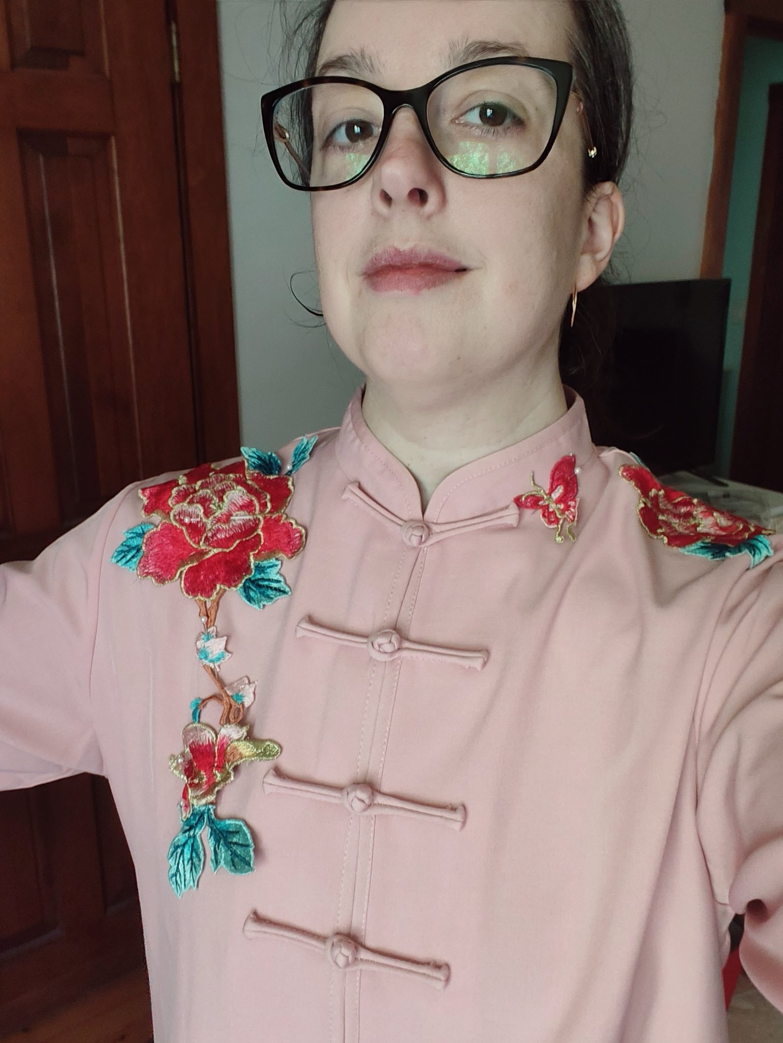 A person is wearing a pink traditional-style garment with colorful floral and butterfly embroidery near the shoulder.