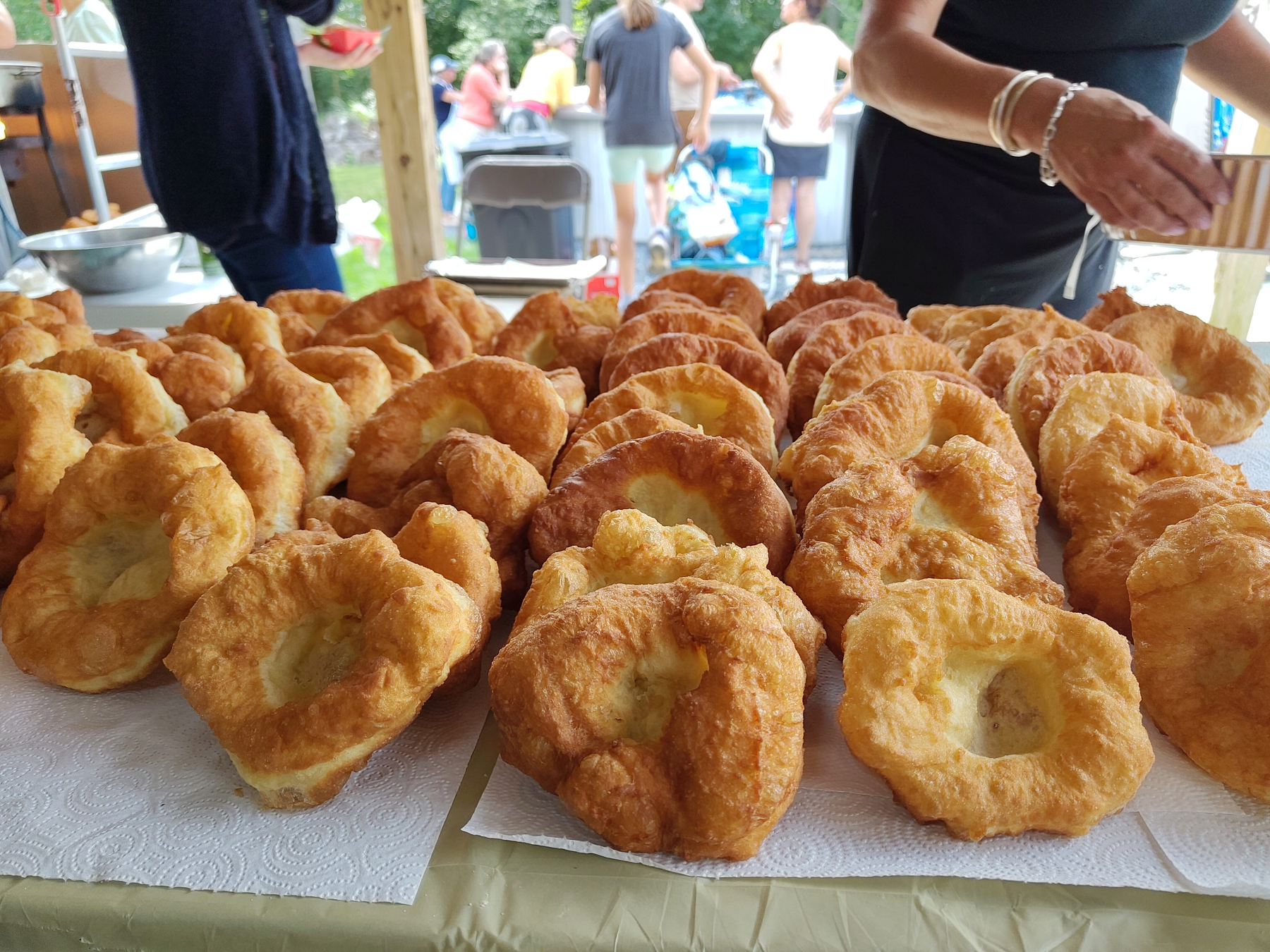 Several rows of golden-brown fried dough pastries are neatly arranged on a table covered with paper towels.