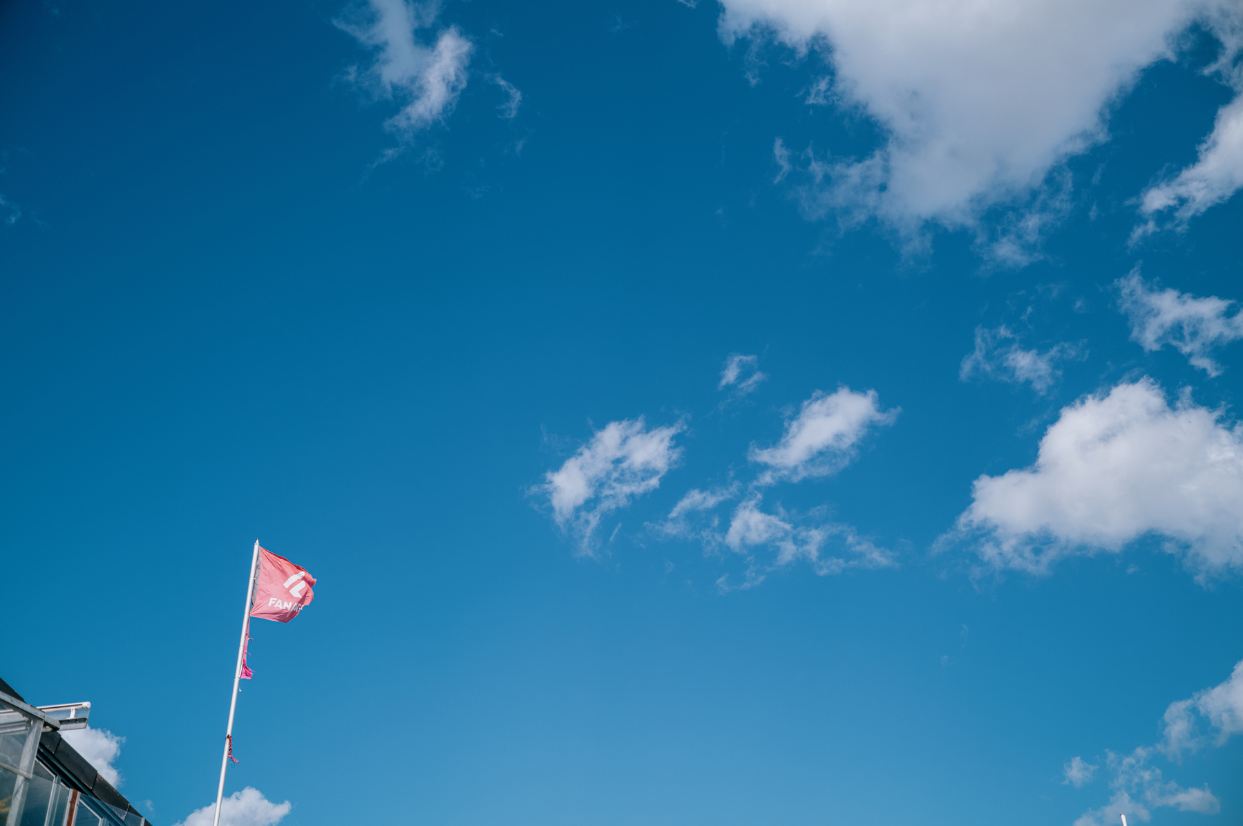 A flag is flying against a clear blue sky scattered with a few white clouds.
