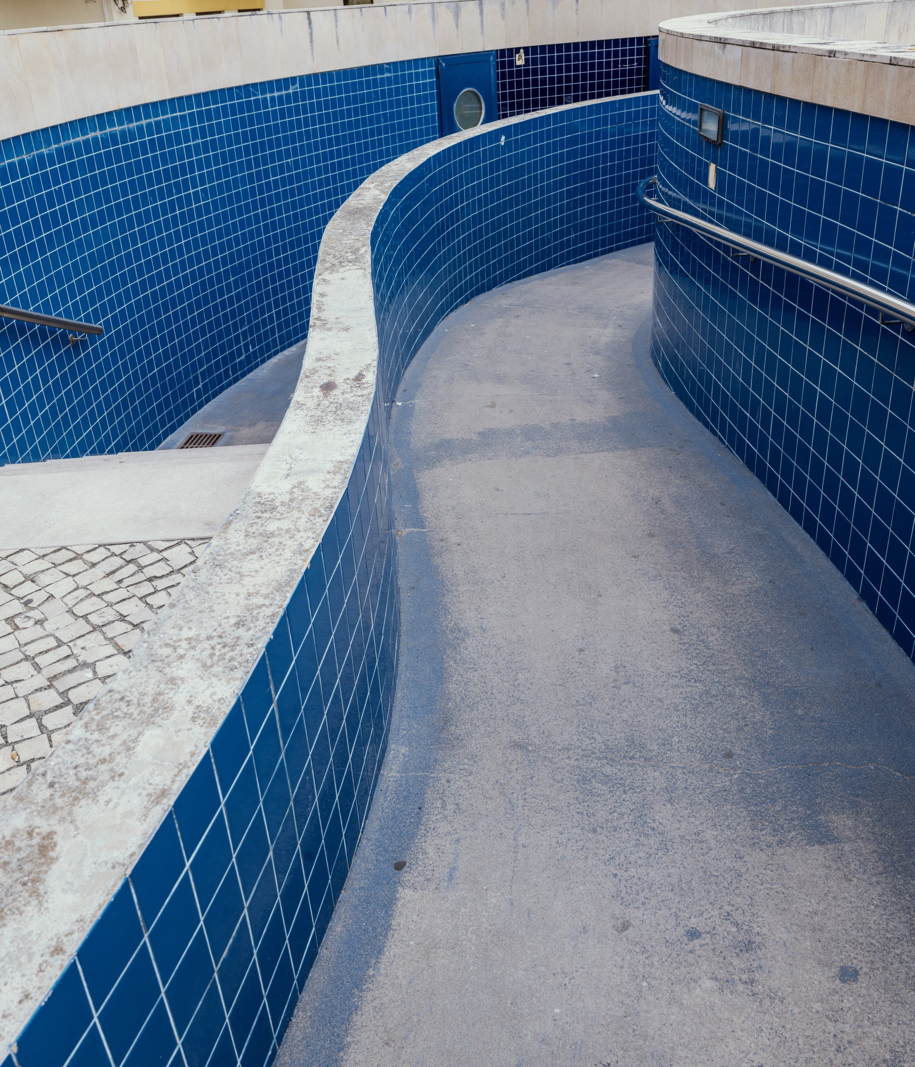 A curving concrete ramp lined with blue tiled walls leads downward, creating a smooth, modern architectural passage.