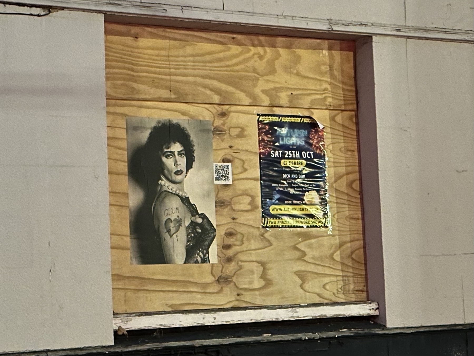 A boarded-up window displays a black-and-white portrait with the word GLAM and a colorful event poster.