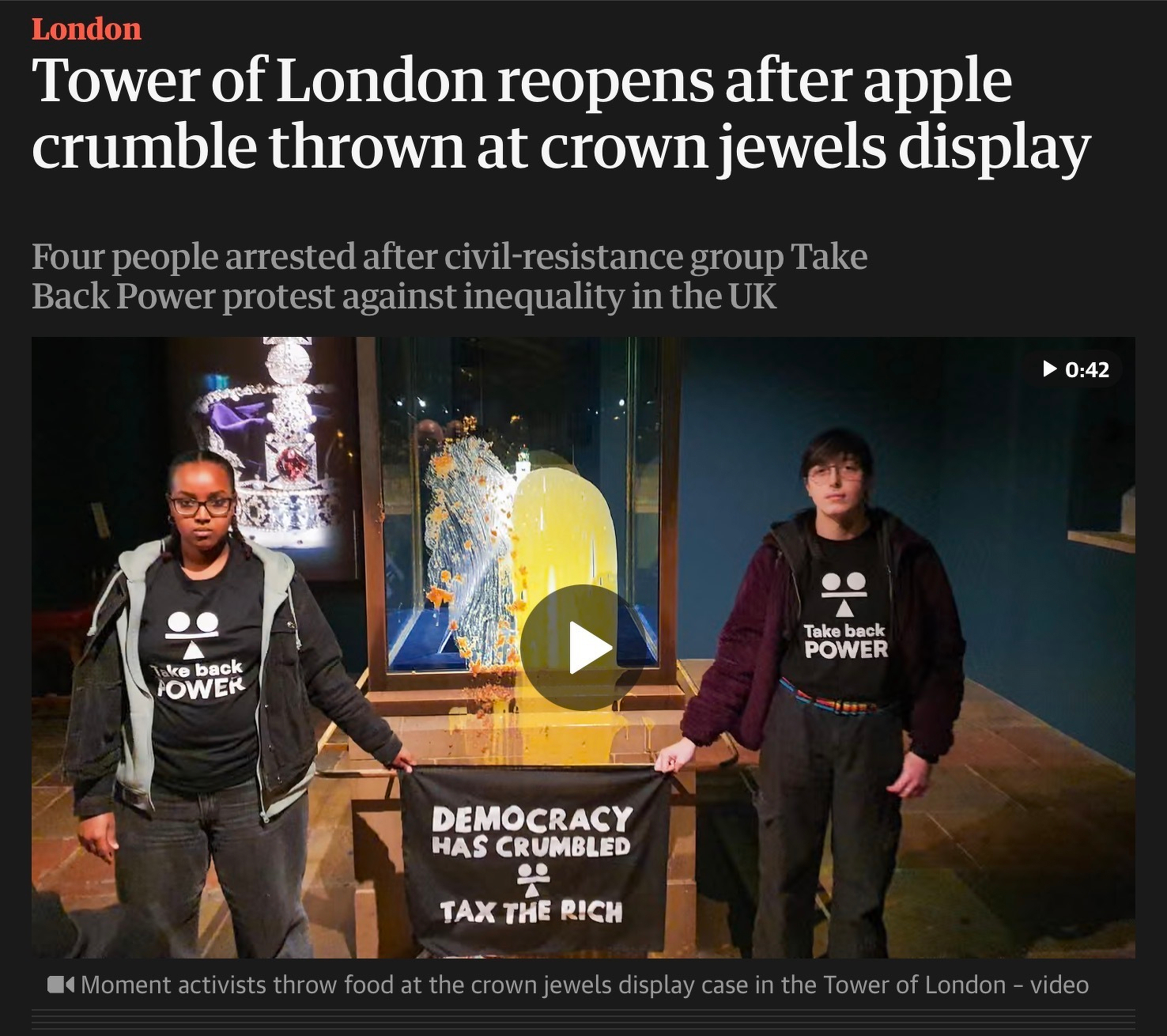 News story of two people wearing Take Back Power shirts stand holding a sign in front of a gate with a cracked case, following an apple crumble protest at the Tower of London. The headline is ‘Tower of London reopens after Apple crumble thrown at Crown Jewels display’