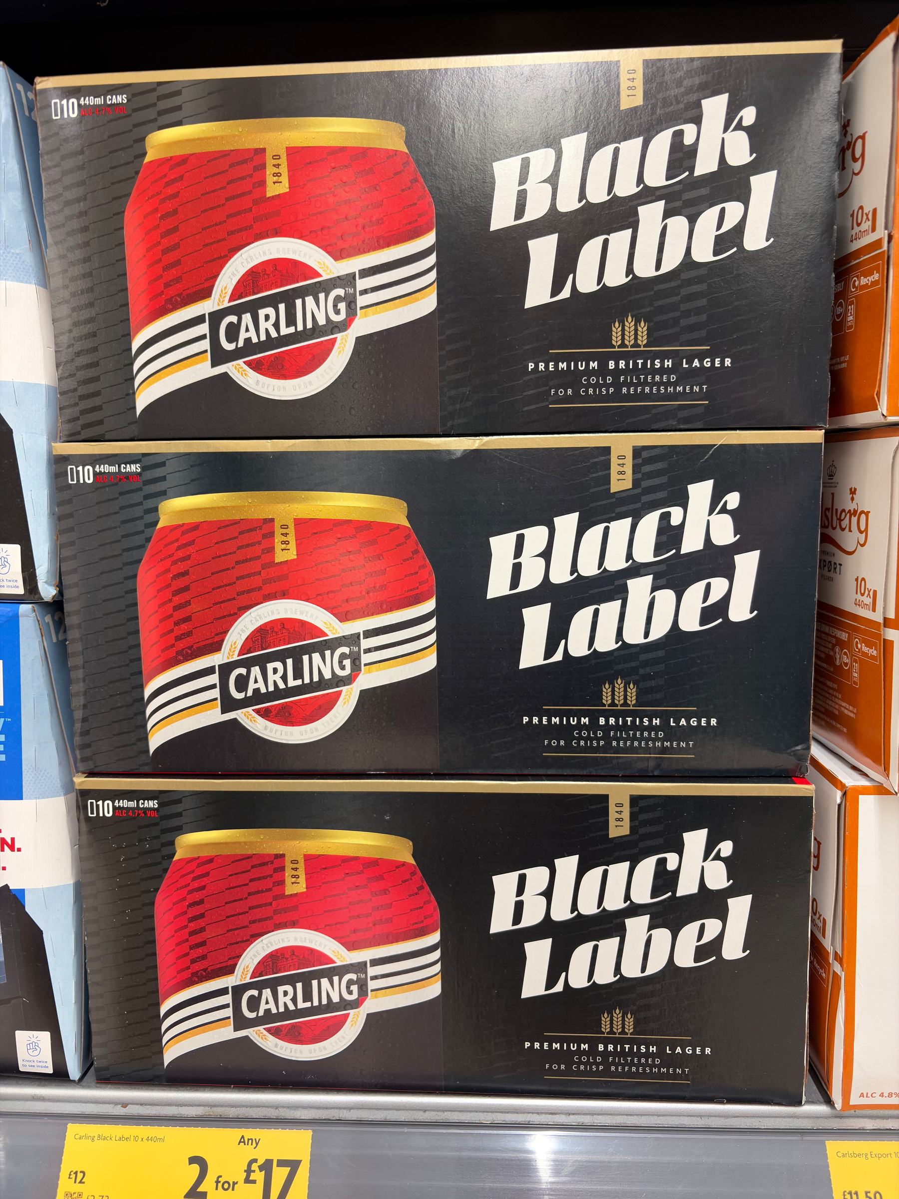 Three boxes of Carling Black Label British Lager are stacked on a shelf.
