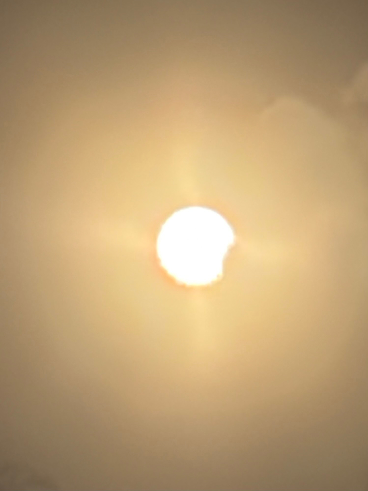 A partial solar eclipse is visible with the sun partially covered by the moon against a hazy sky.