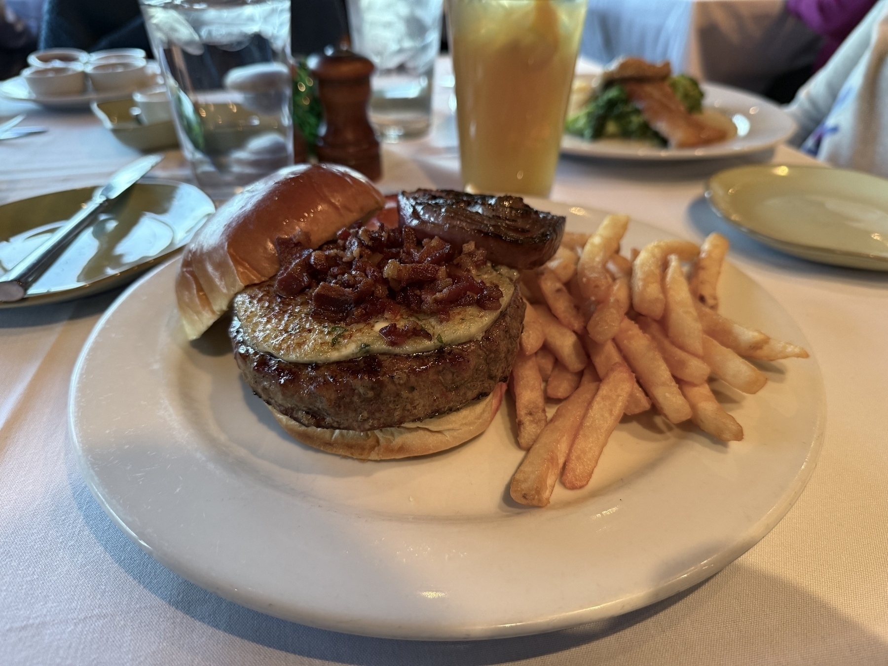 Auto-generated description: A burger topped with bacon is served on a plate with fries.