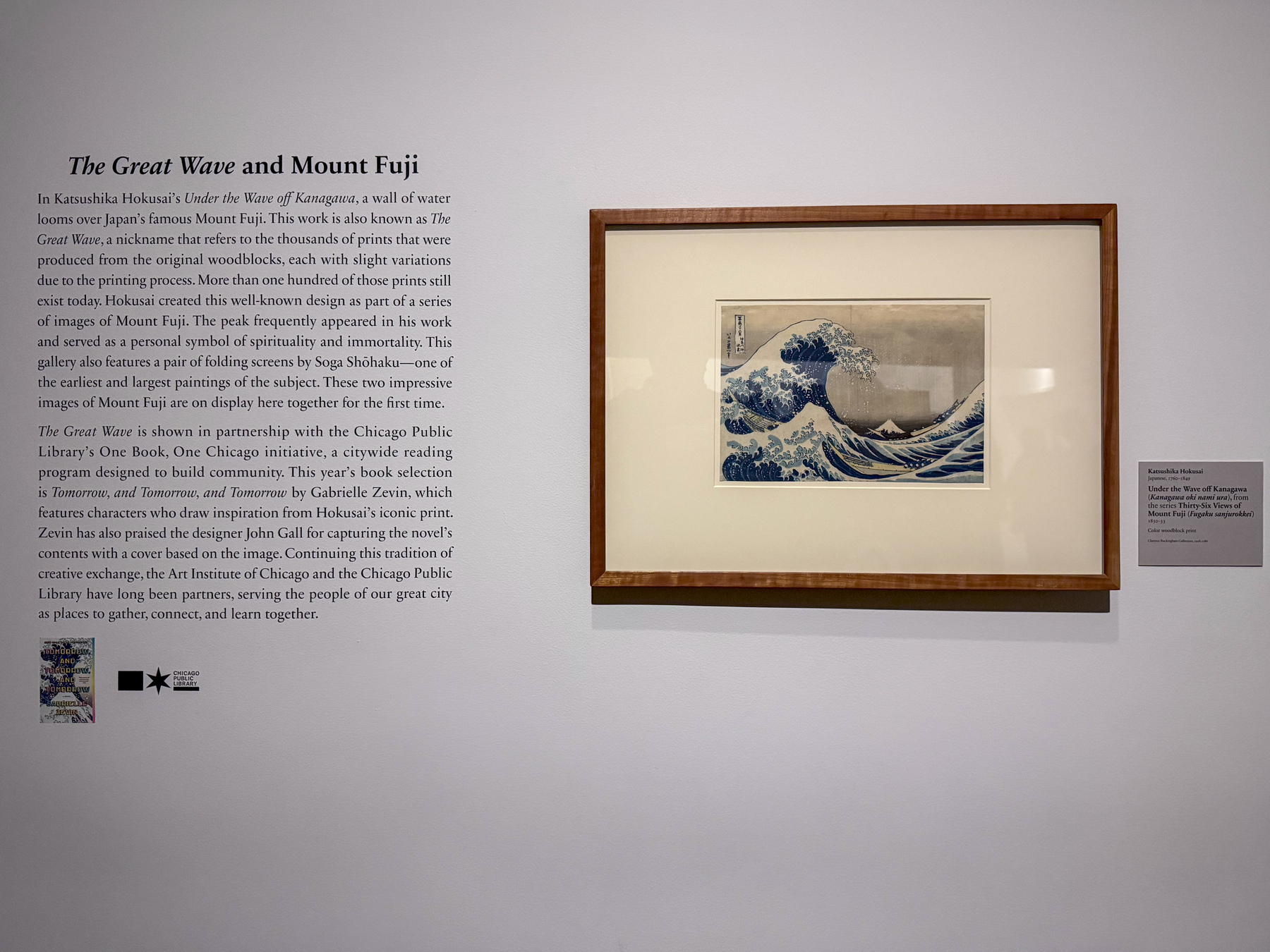 Auto-generated description: A framed artwork depicting Hokusai's famous The Great Wave is displayed on a wall with descriptive text explaining its significance and origins.