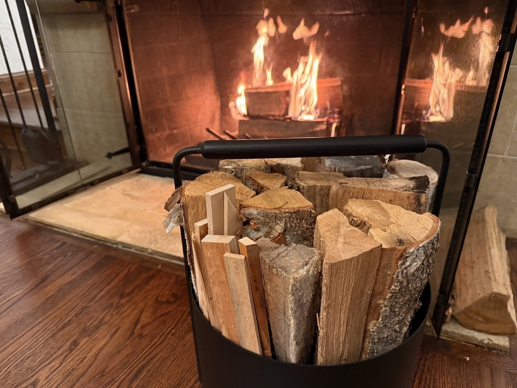 Auto-generated description: A cozy fireplace burns brightly in the background with a basket of firewood placed in the foreground.