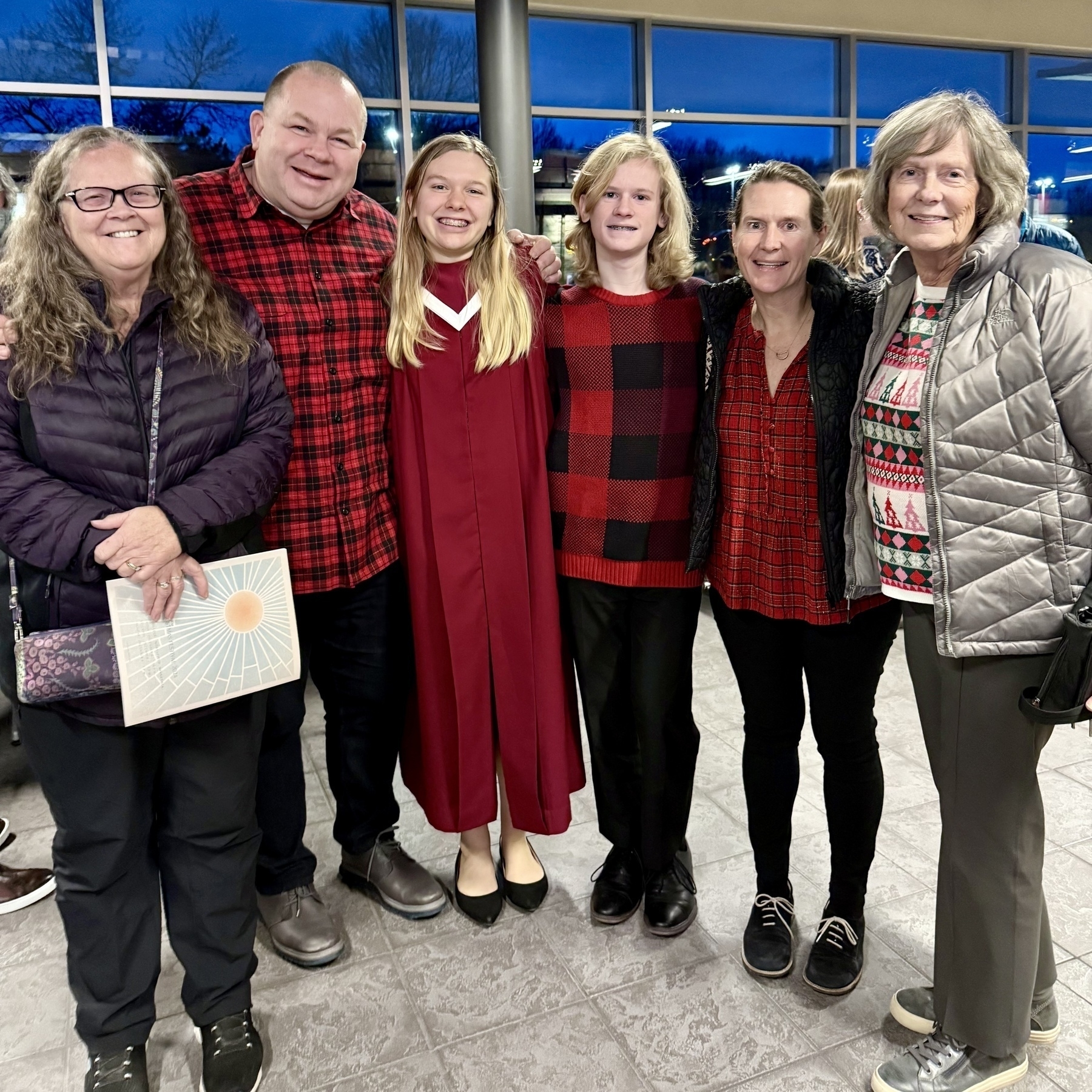 Auto-generated description: A group of six people, including two individuals wearing red plaid shirts and one in a maroon robe, happily gather indoors for a photo.