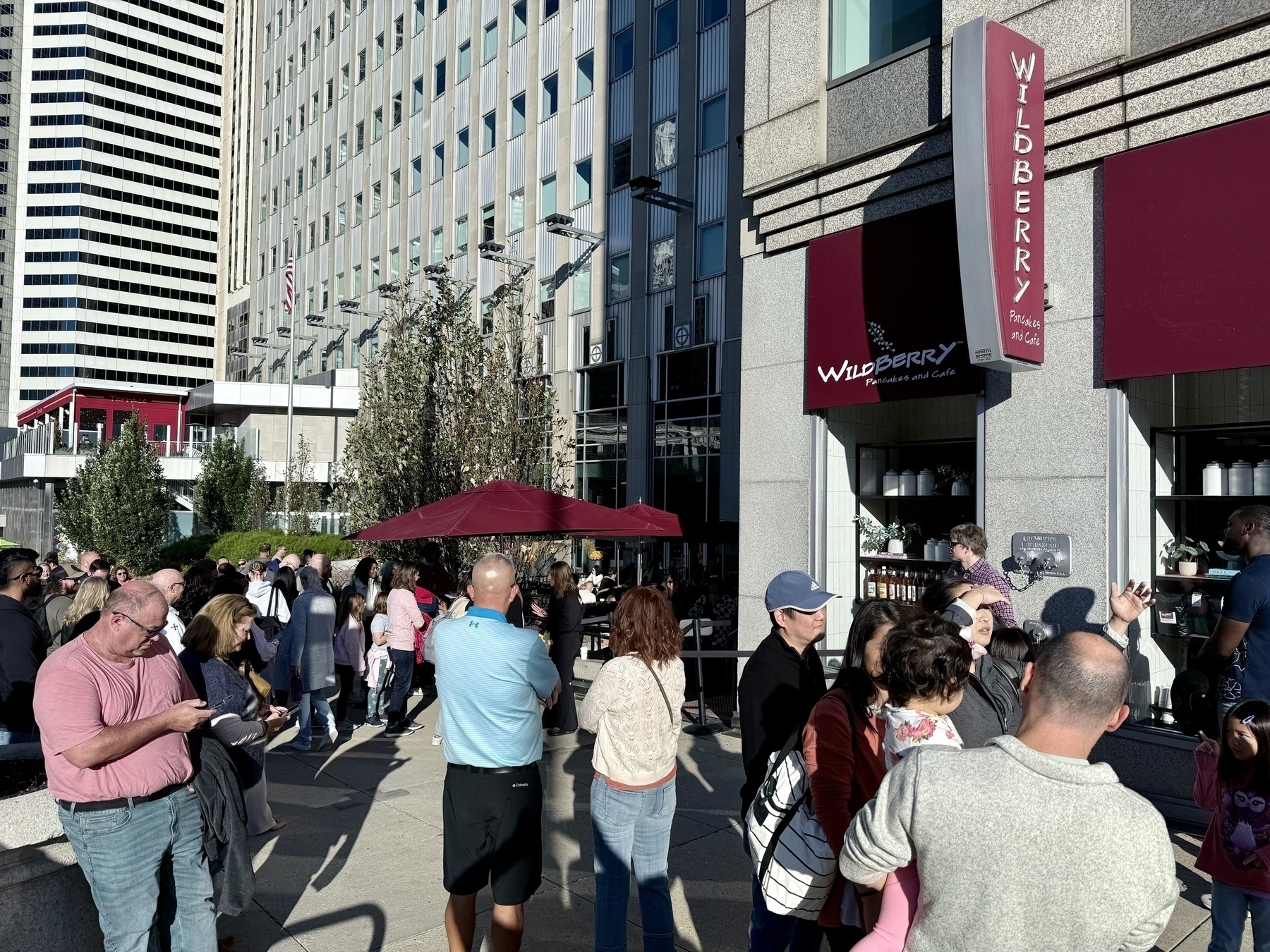 Auto-generated description: People are lined up in front of a popular restaurant called Wildberry waiting to get inside, with skyscrapers in the background.