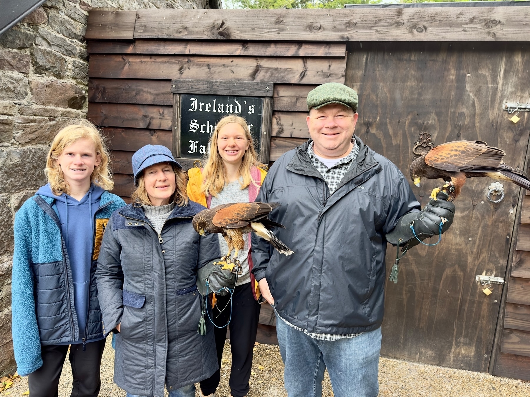 Auto-generated description: A group of four people, one child, and three adults are smiling while holding birds of prey at Ireland's School of Falconry.