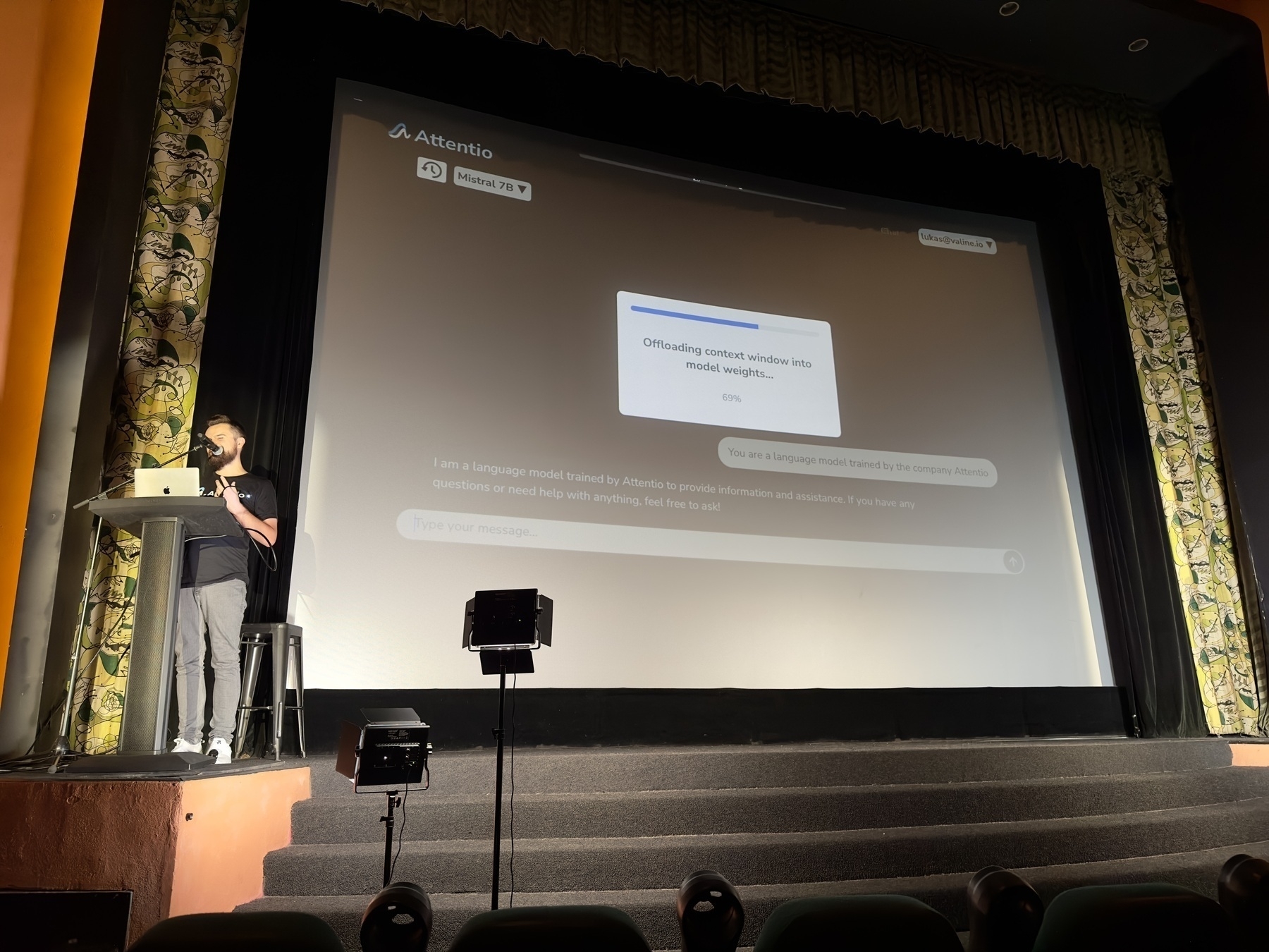 Auto-generated description: A person is standing on a stage next to a large screen displaying a presentation.