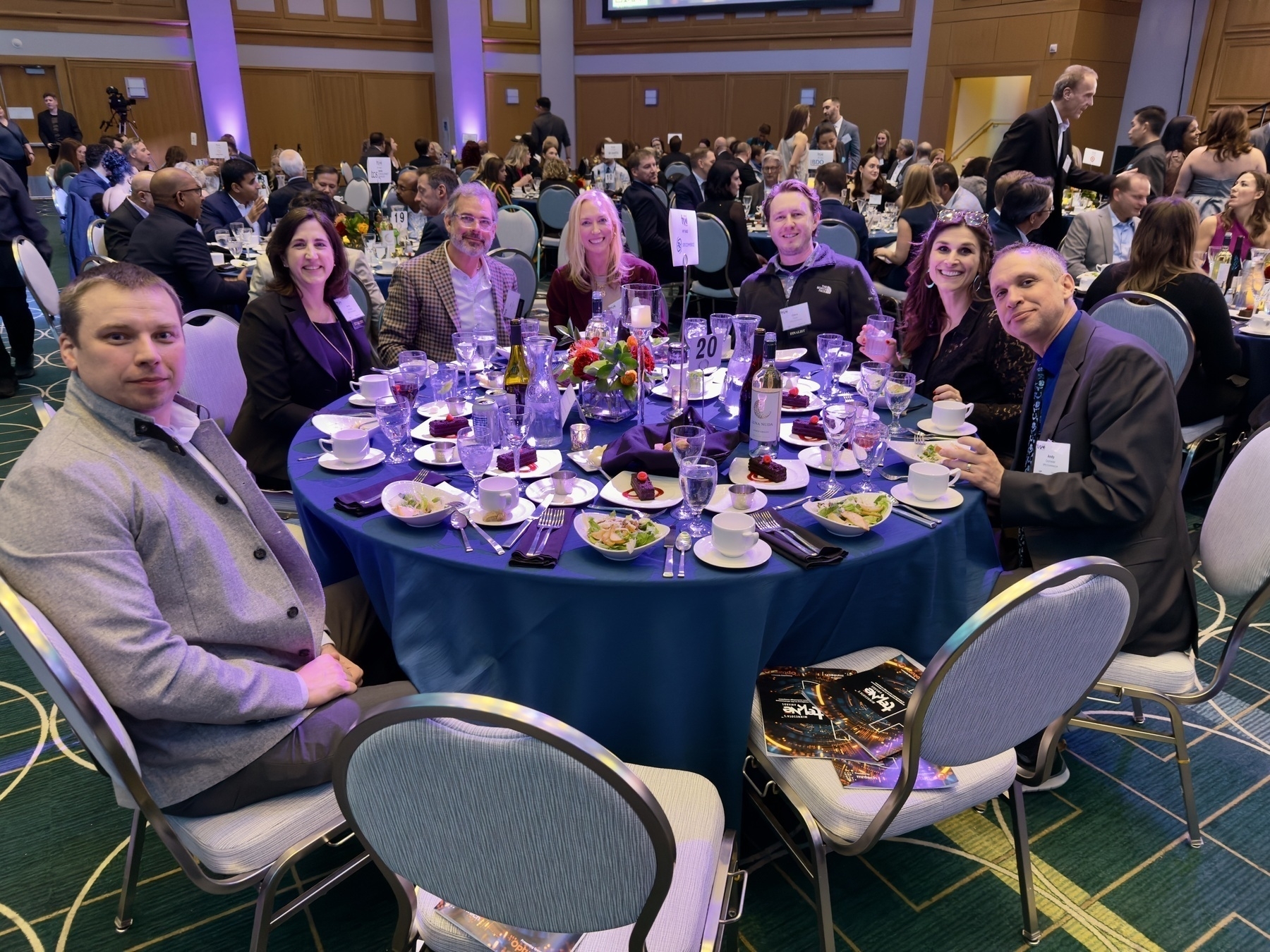 Auto-generated description: A group of people are sitting around a table at a formal event, surrounded by plates, glasses, and decorations.