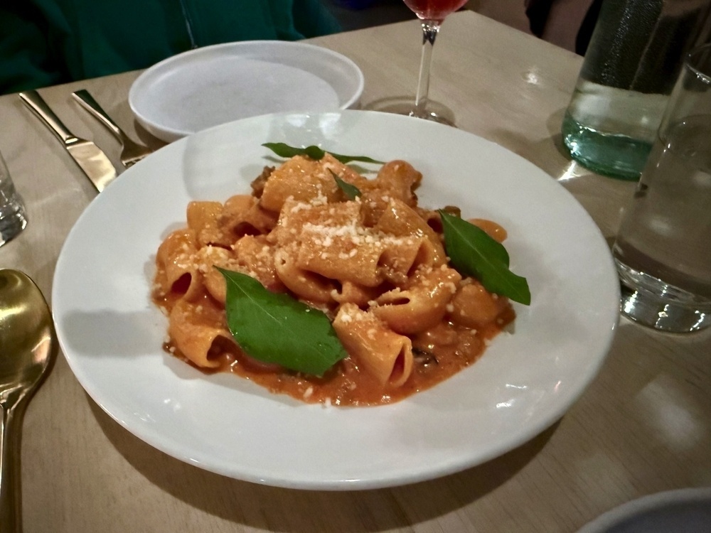 A plate of pasta topped with sauce, garnished with fresh basil and grated cheese, is set on a dining table.