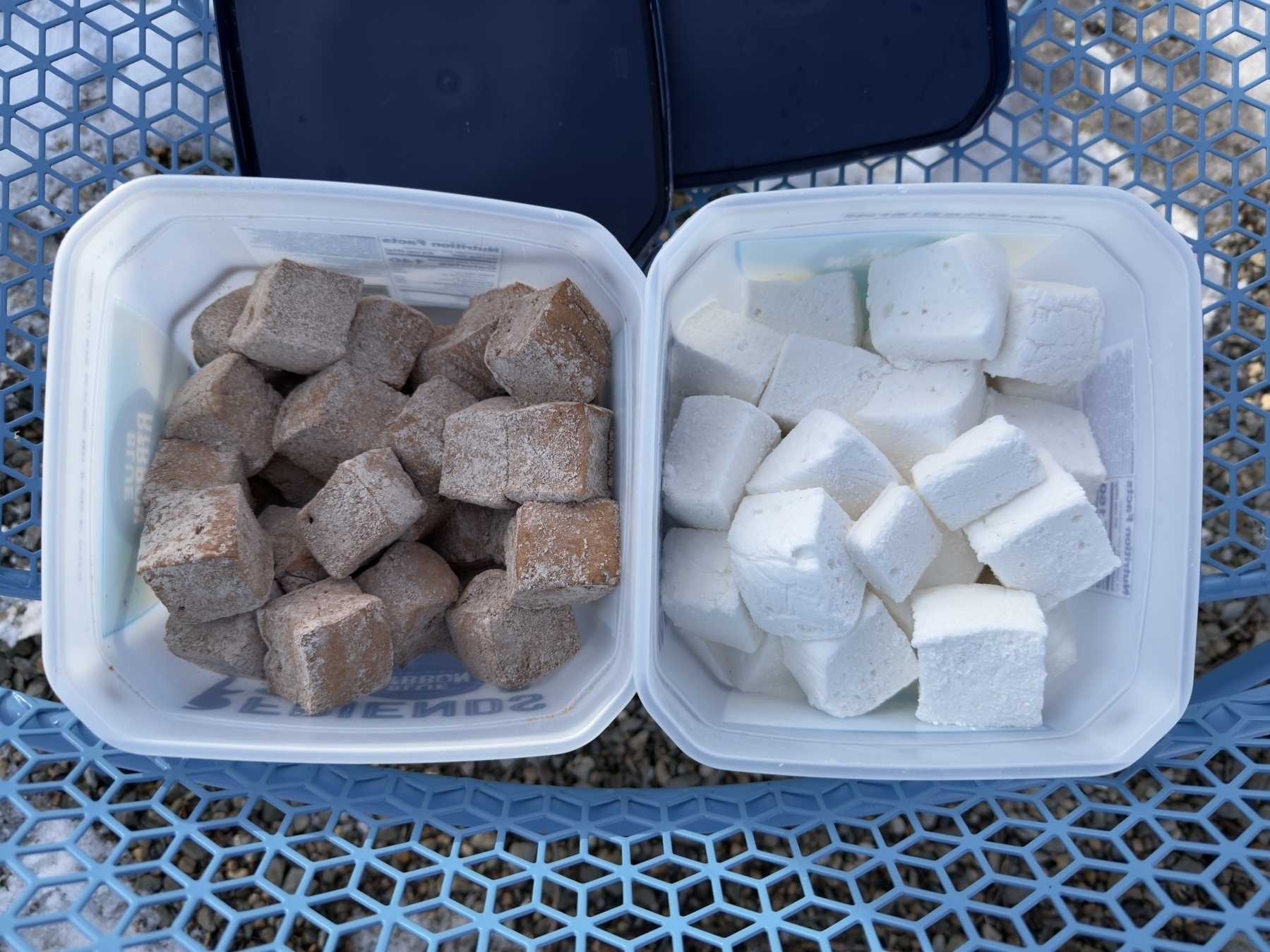 Two containers hold brown and white cubes, placed on a blue mesh surface.