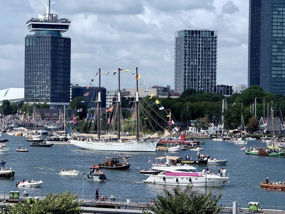 Numerous boats are gathered on a river, surrounded by tall buildings and a crowd of spectators.