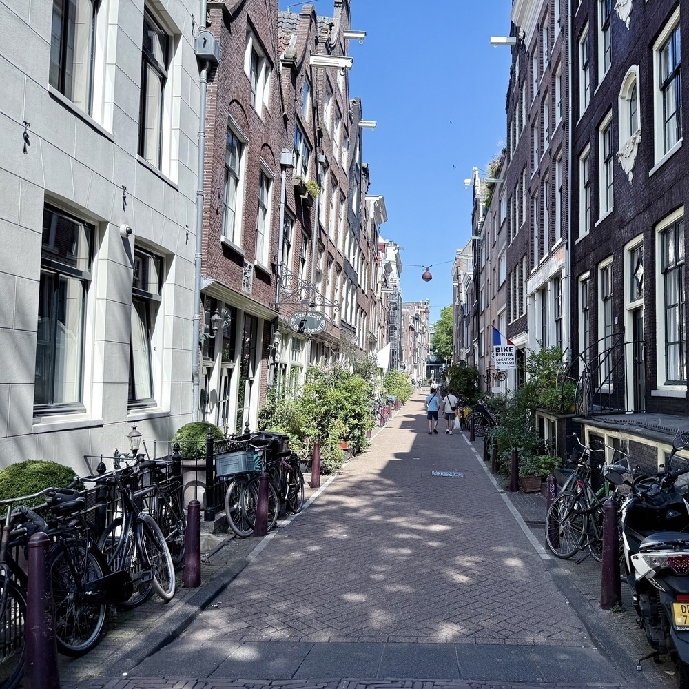 A narrow street lined with old European buildings features rows of bicycles parked on both sides.