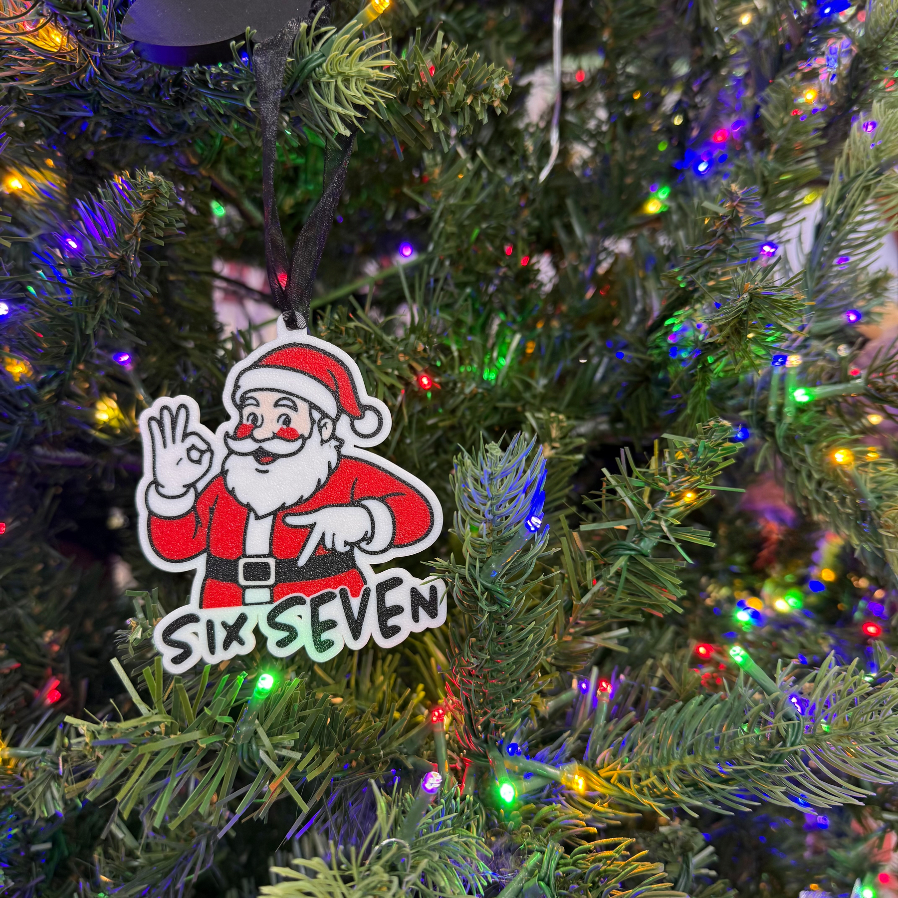 A Christmas tree is decorated with colorful lights and an ornament featuring Santa Claus making an OK gesture and the text SIX SEVEN.