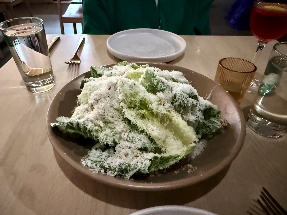 A plate of greens topped with shredded cheese is served on a table set with glasses and utensils.