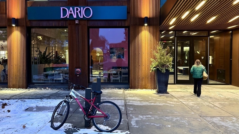 A bicycle is parked in front of the Dario restaurant entrance, where a person wearing a green jacket is walking inside.