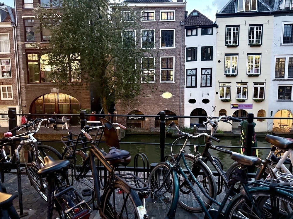 Bicycles are parked along a canal with a backdrop of historic buildings.