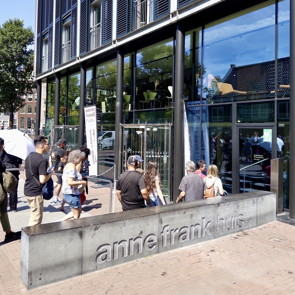People are lined up outside the Anne Frank House, a modern building with large glass windows.