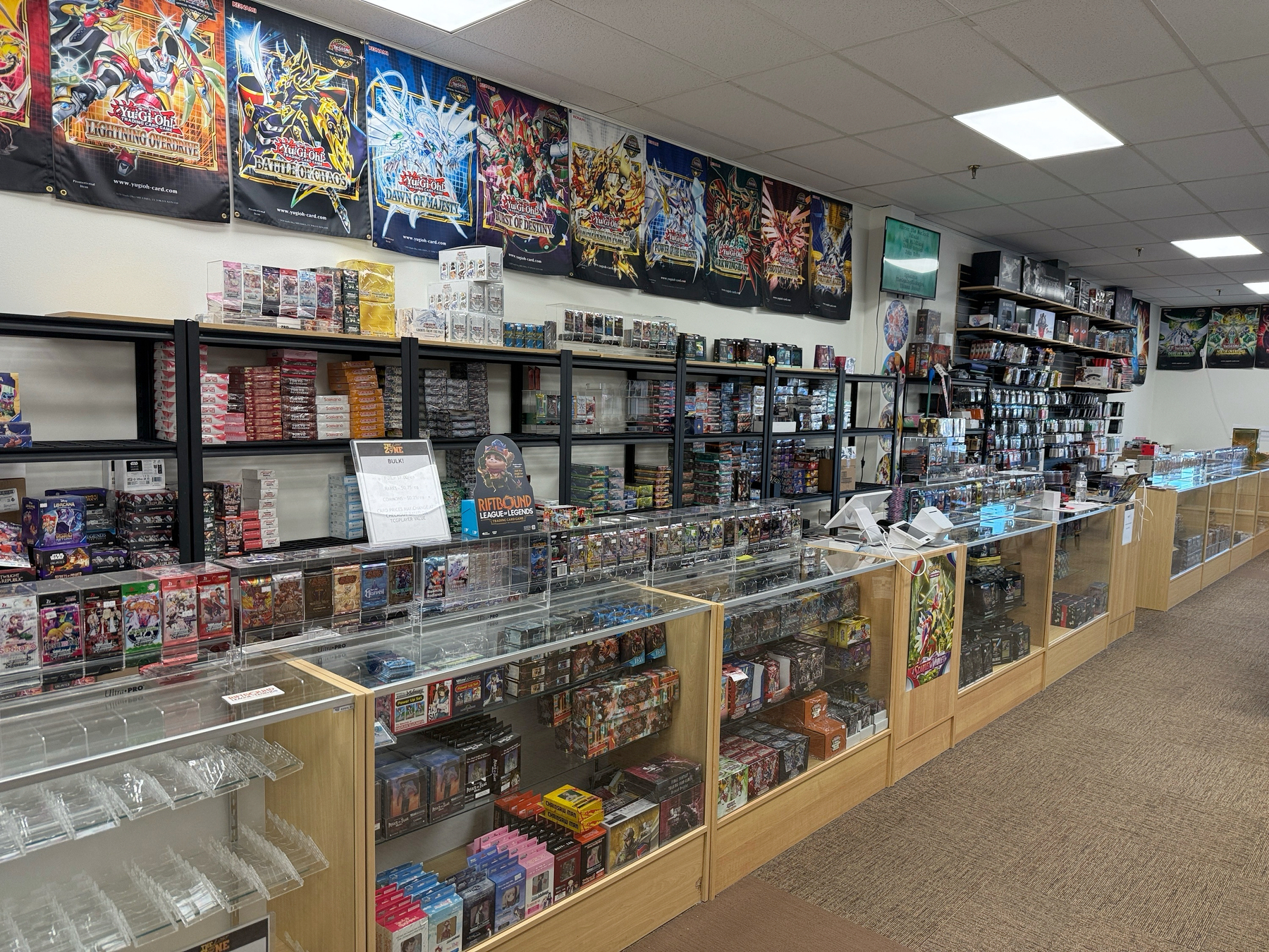 A store is filled with display cases and shelves showcasing a wide variety of trading card game products and accessories.