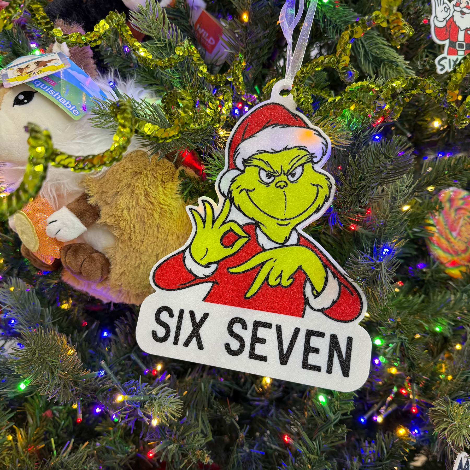 A festive Christmas tree is decorated with plush toys, ornaments, and a Grinch-themed sign with the words SIX SEVEN.