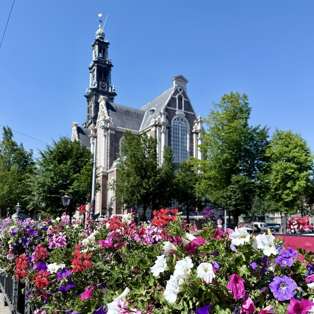 A historic church stands majestically amidst vibrant flowers and lush green trees under a clear blue sky.
