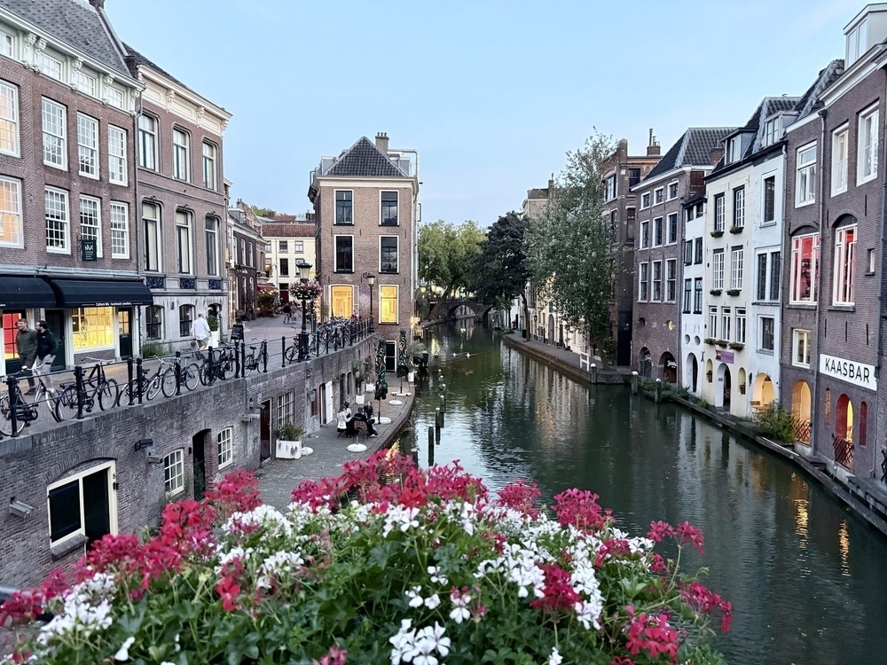 A picturesque canal is bordered by historic buildings and adorned with vibrant flowers in the foreground.