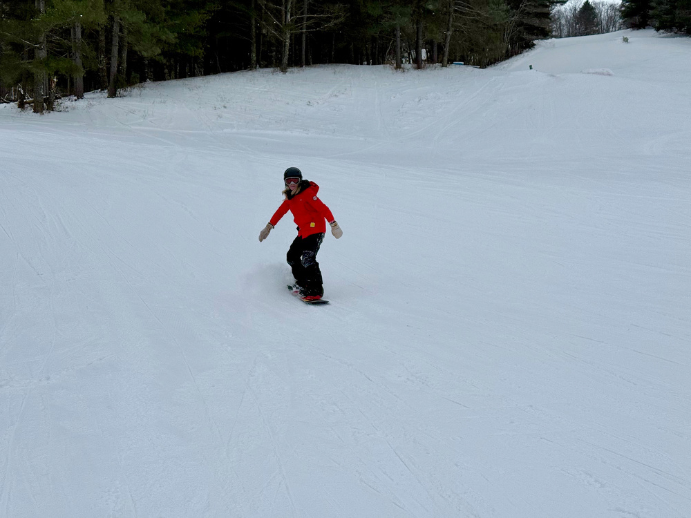 A person is snowboarding down a snowy slope surrounded by trees.