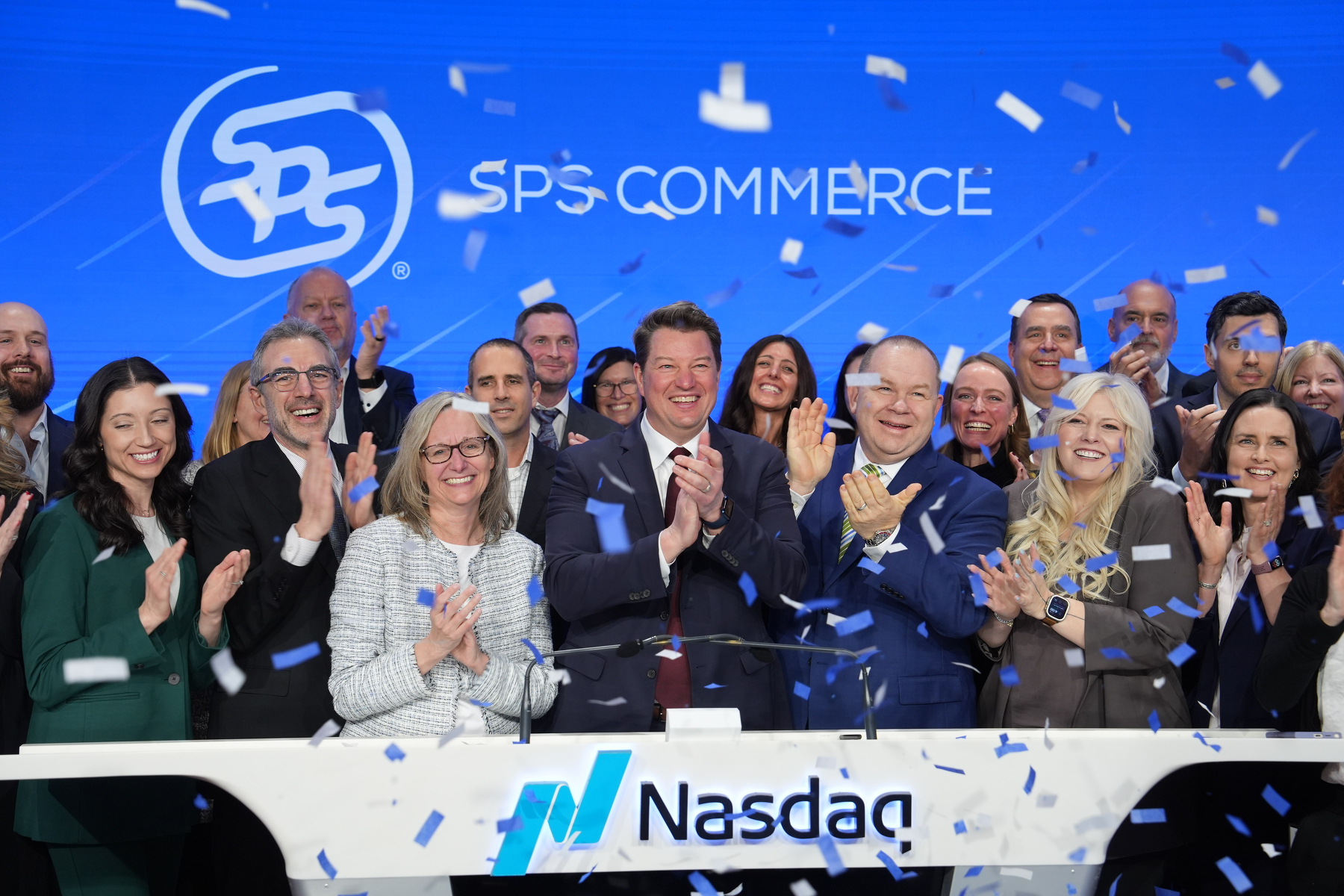 A group of people is celebrating an event at the Nasdaq with confetti falling in a festive atmosphere.