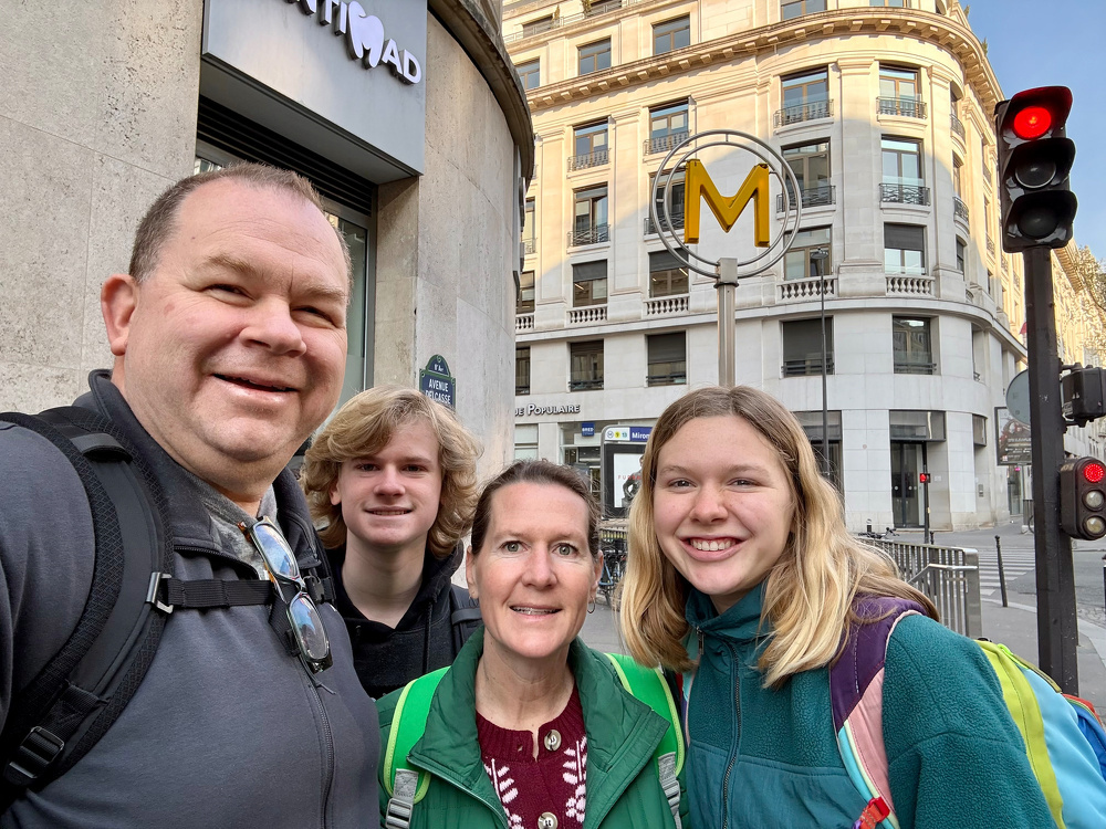 A family of four is smiling in front of a building with a metro sign in a city setting.