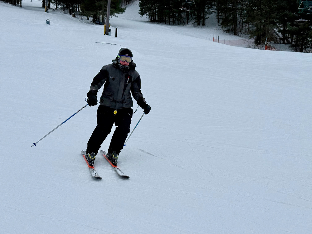A person is skiing down a snowy slope wearing winter gear and holding ski poles.