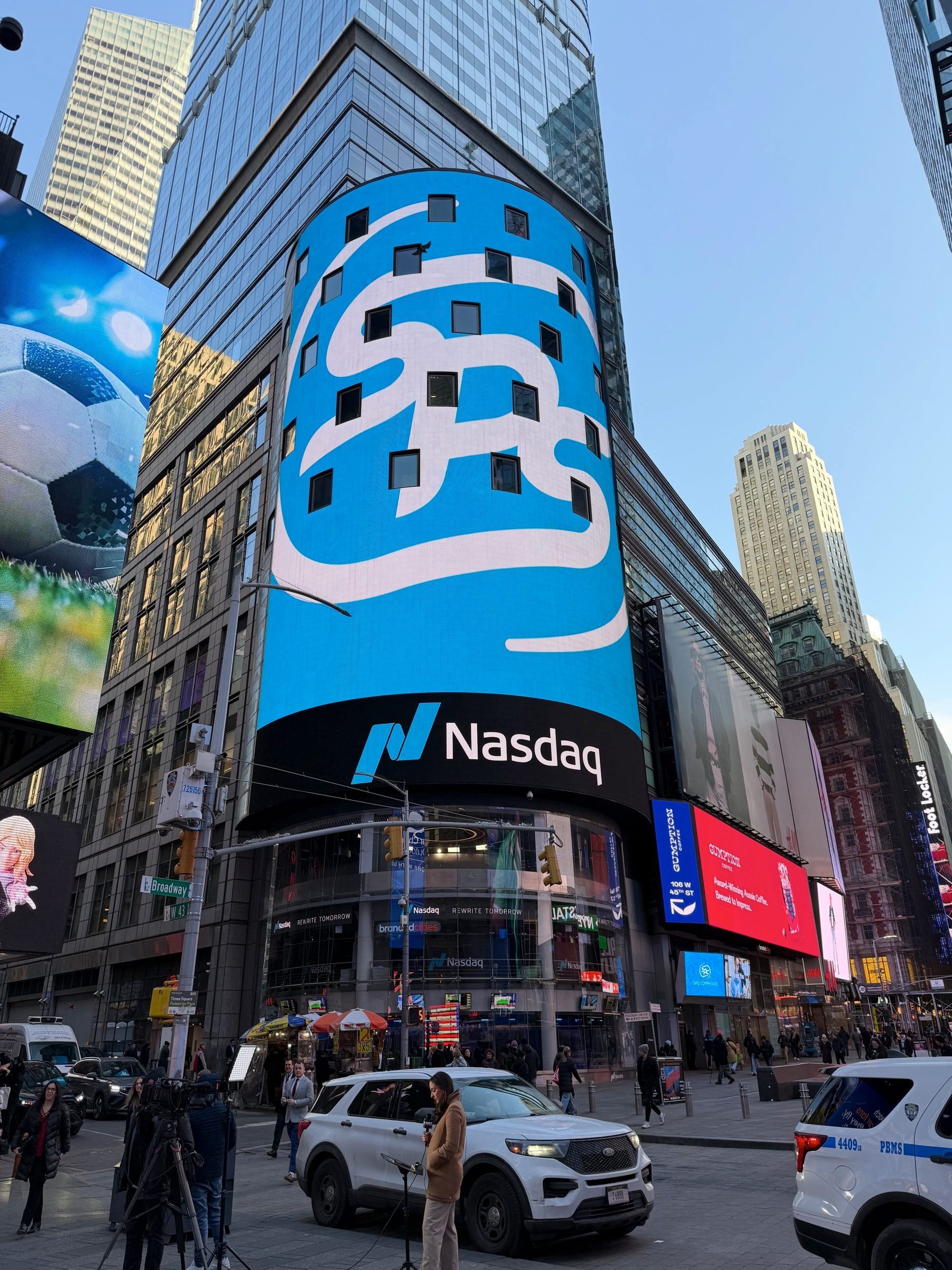 A busy street scene features the Nasdaq building in Times Square, displaying a large digital screen with its logo.