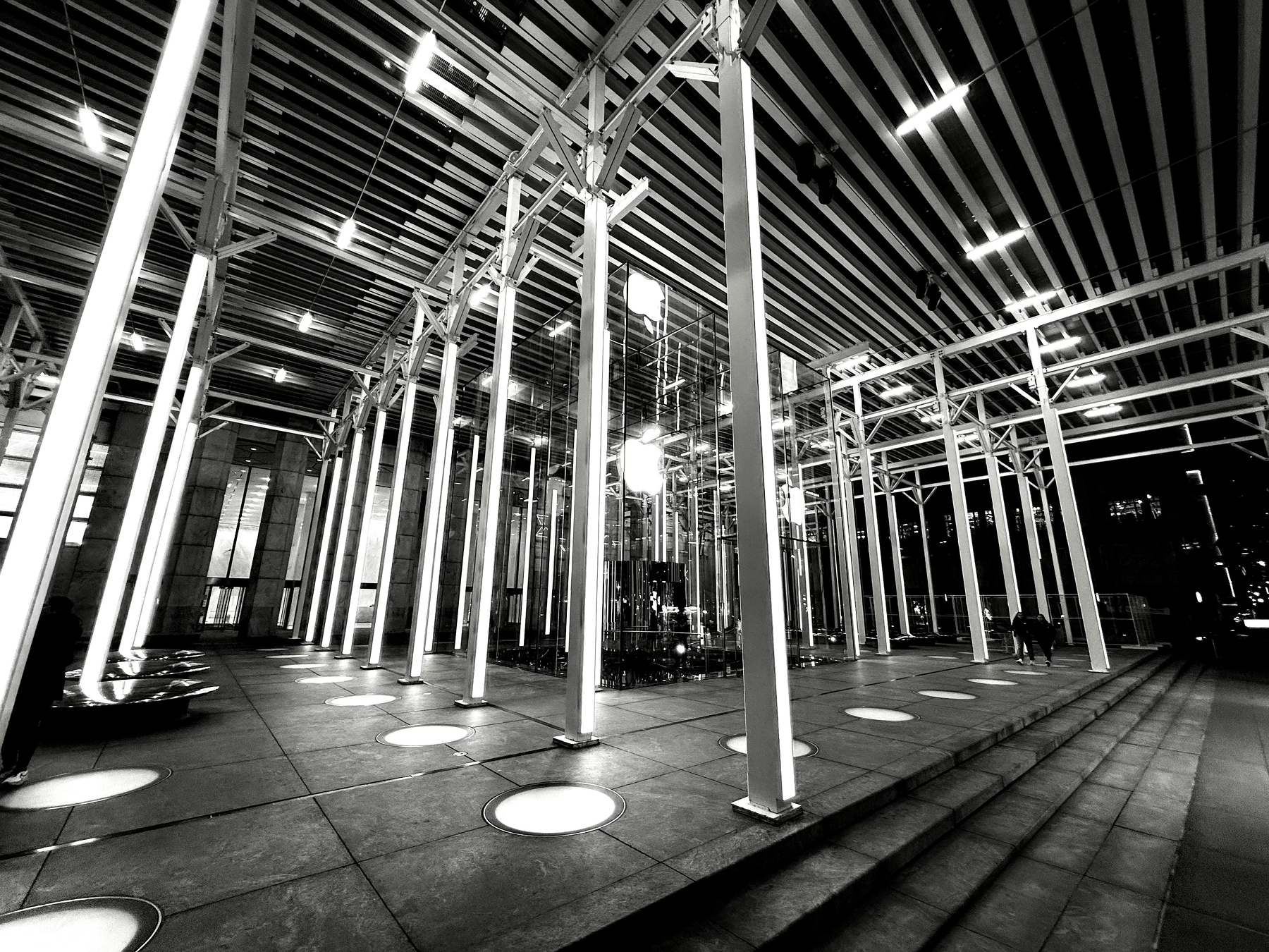 Auto-generated description: A modern architectural structure features a series of illuminated vertical beams and a grid-like ceiling, creating a striking and futuristic atmosphere.