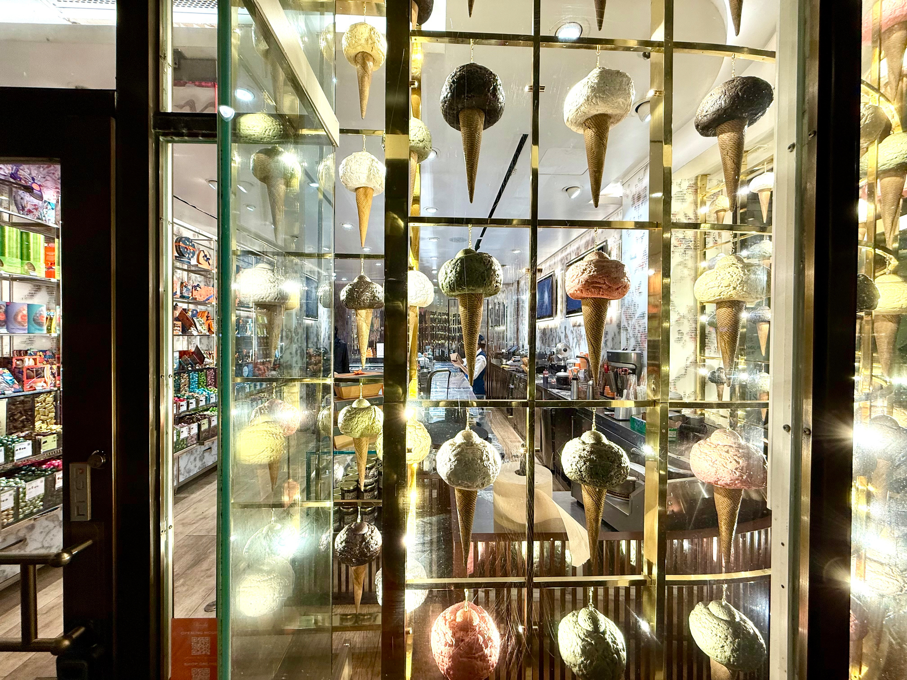 Auto-generated description: A shop window displays large, colorful ice cream cone models, lit up and arranged on a grid, with a view inside revealing various products.