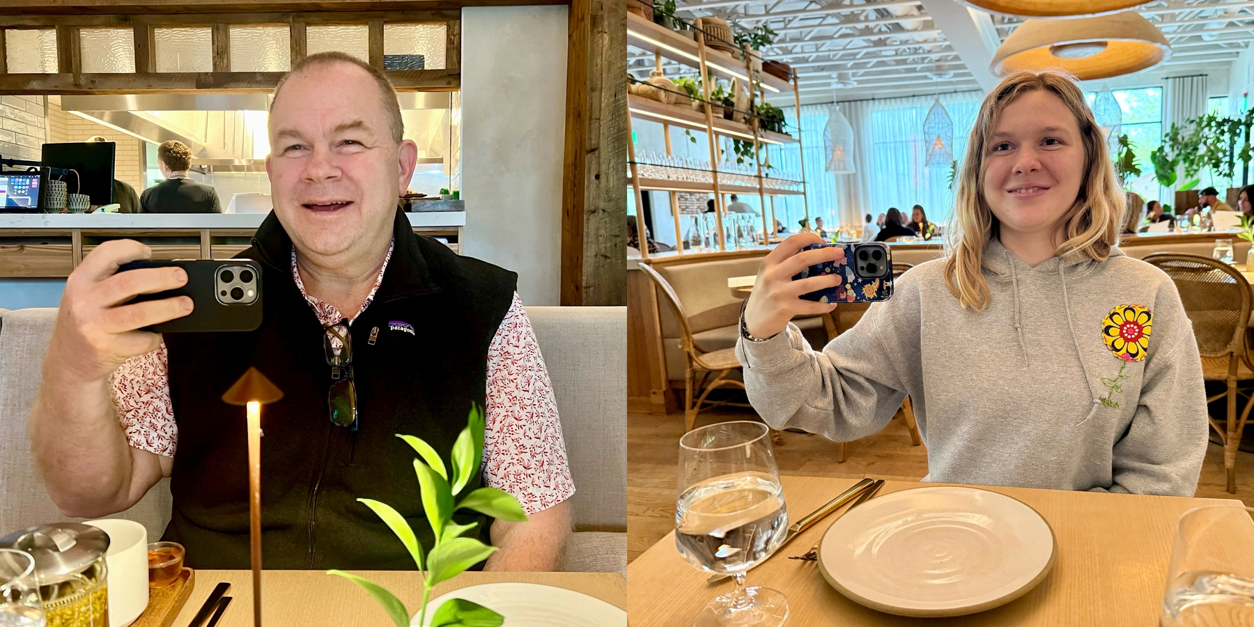 Two people at separate restaurant tables, each holding up a phone to take a photo, smiling at the camera.