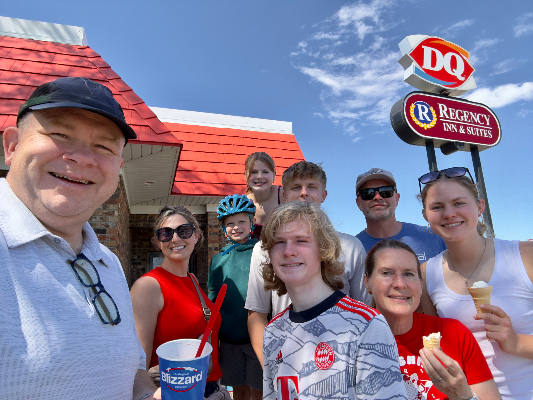 Group of people smiling outside a Dairy Queen holding Blizzard cups and ice cream cones on a sunny day.