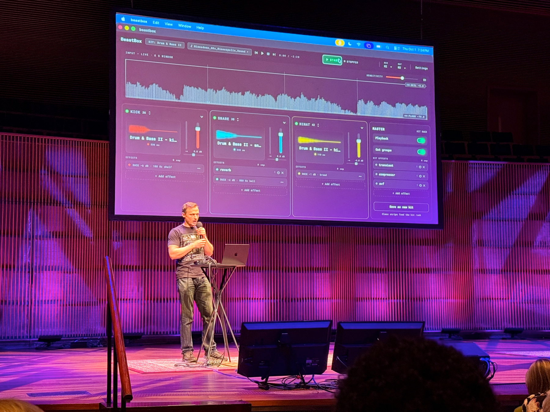 A man with a microphone stands at a laptop on stage while a screen shows BeastBox, a drum app with kick, snare and hihat tracks.