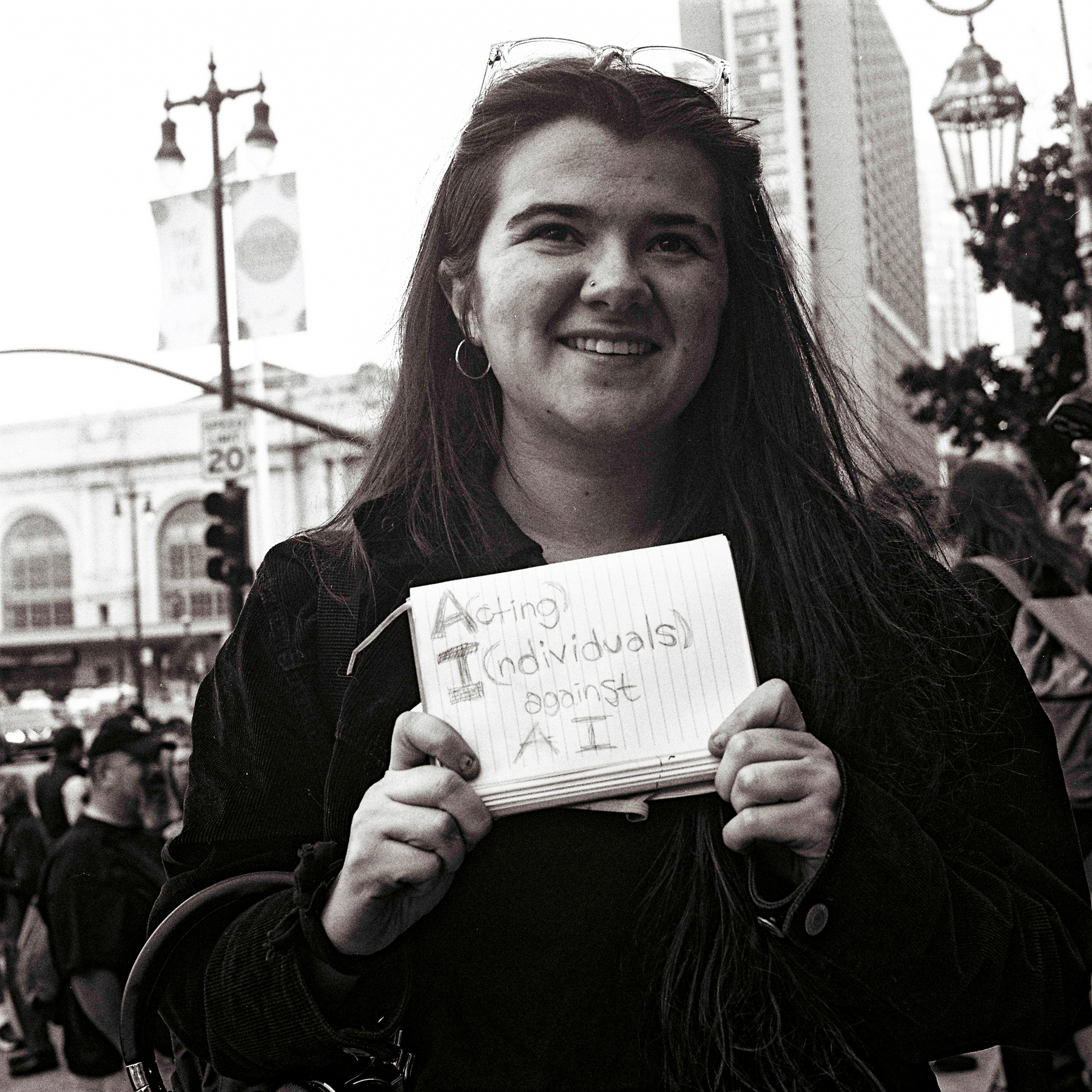 a scan of a black and white photo showing a woman holding a handmade sign written on a piece of ruled paper that says A(cting) I(ndividuals) Against AI