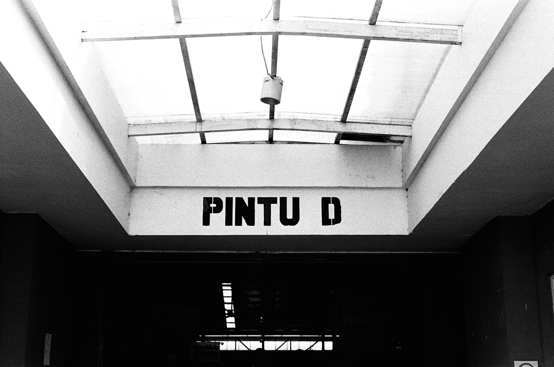 a scan of a black and white photo of a door and skylight windows from inside a wet market. it says Pintu D, which is Indonesian for Door D