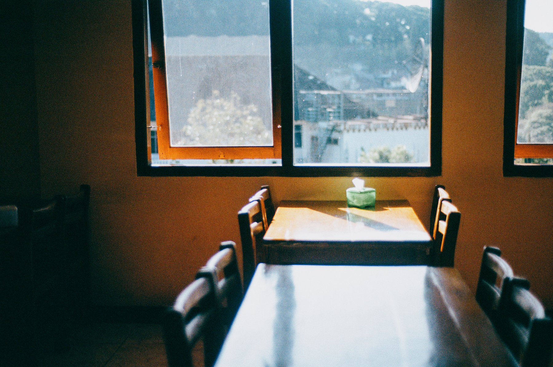 2. a scan of a color photo of wooden tables inside a restaurant that is slightly dark, with sunlight streaming onto a table that has a tissue paper box