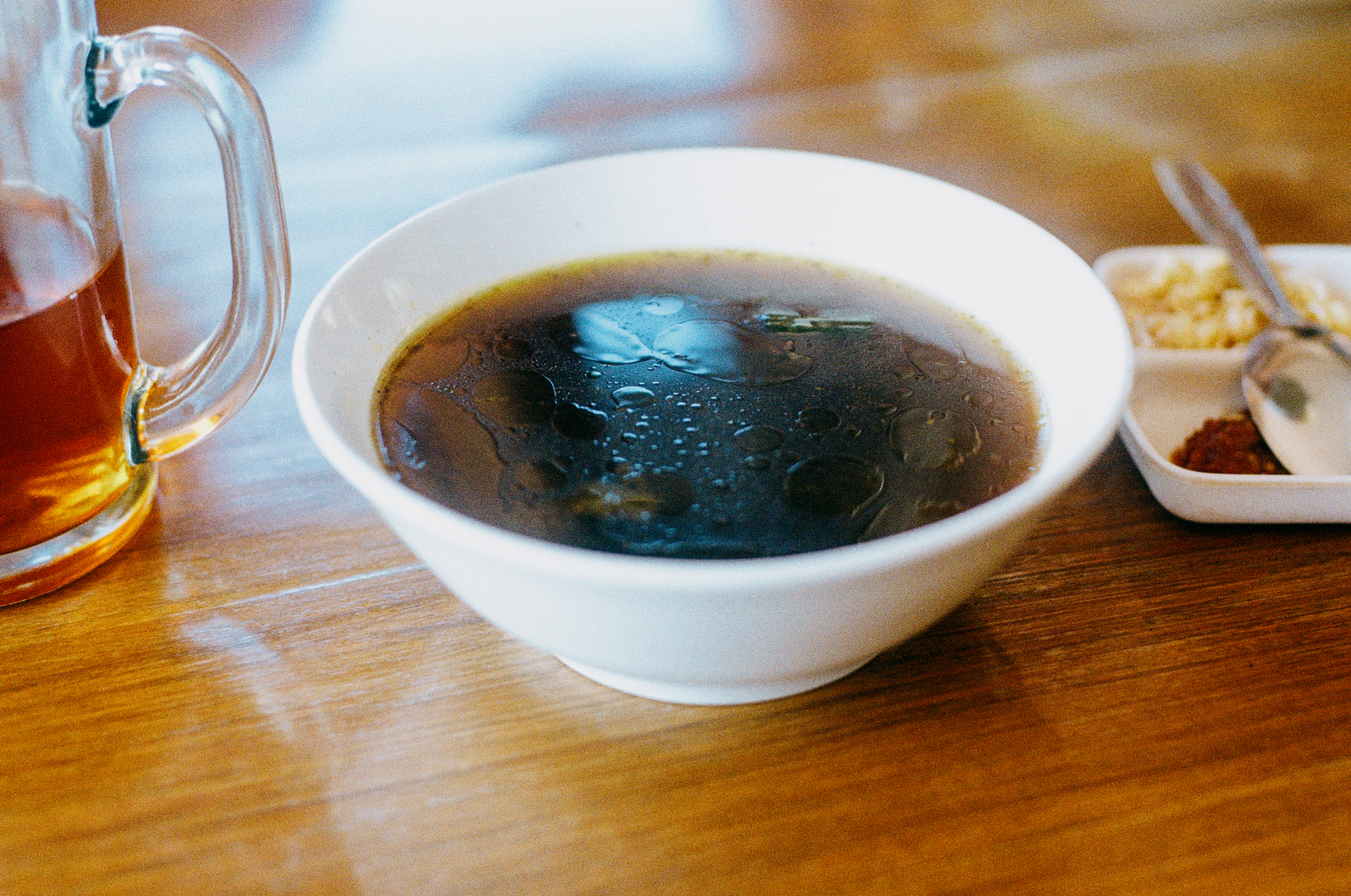 a scan of a color photo of rawon, an Indonesian beef soup, on a wooden table with tea