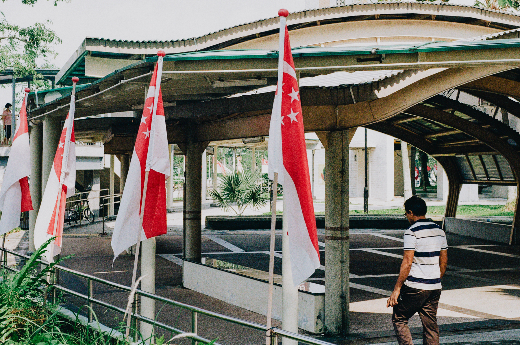 a scan of a color photo of a few singapore flags on poles at a covered walkway