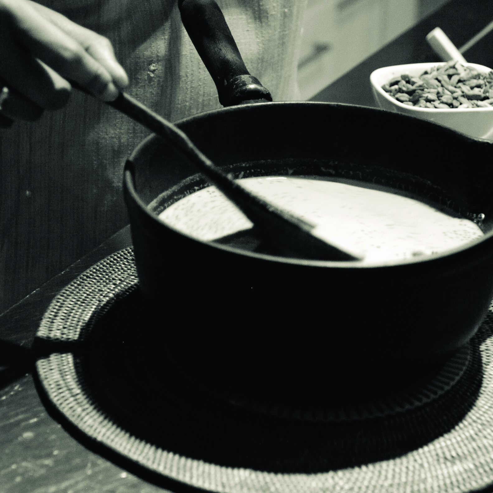 A black and white photo of a cast iron cauldron with milk in it, and someone stirring