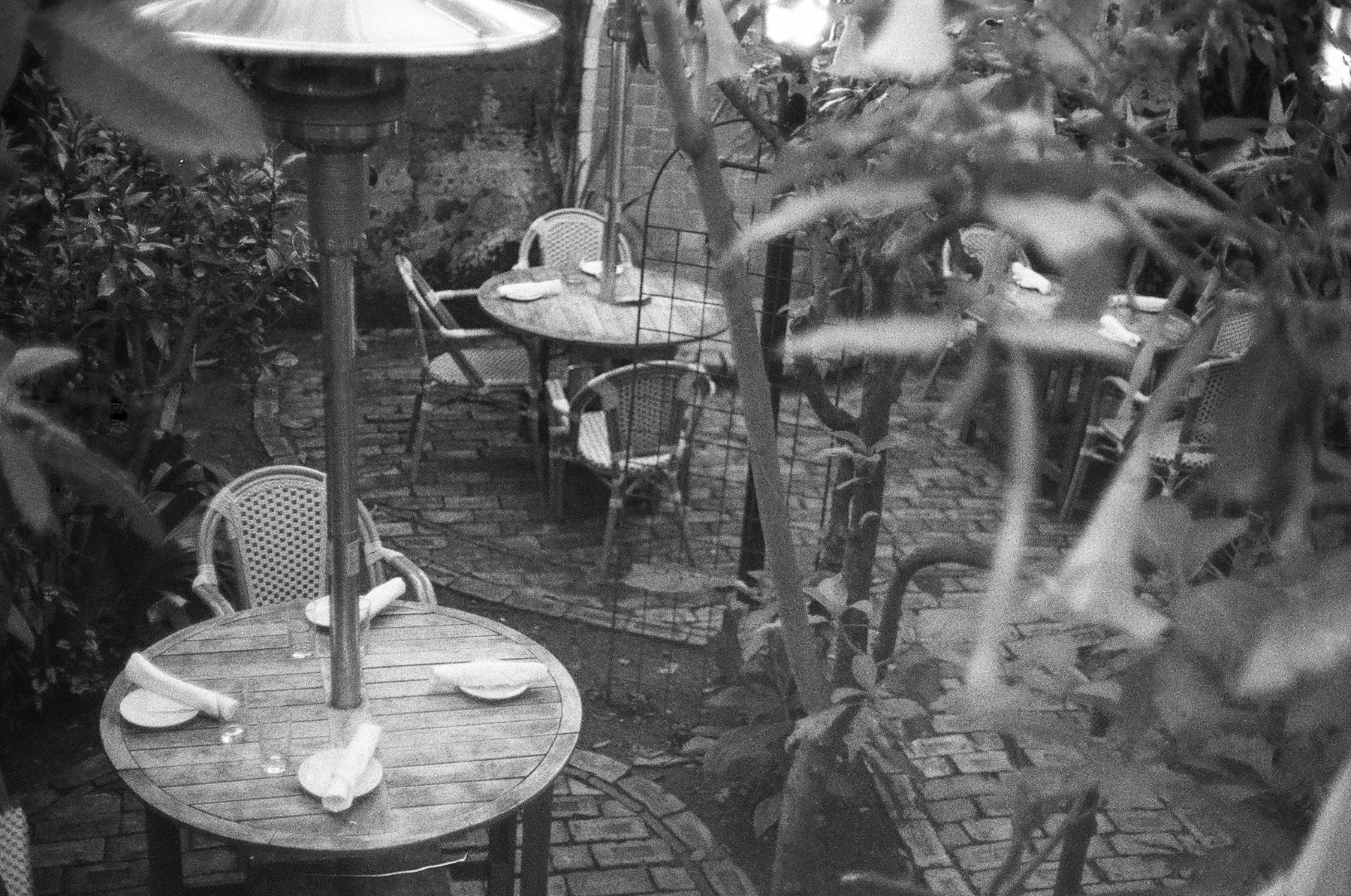 a scan of a black and white photo showing an outdoor garden dining space with space heaters