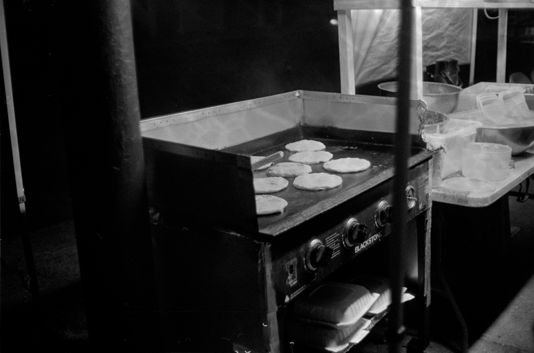 a scan of a black and white photo showing a few pupusas being cooked on a flat grill
