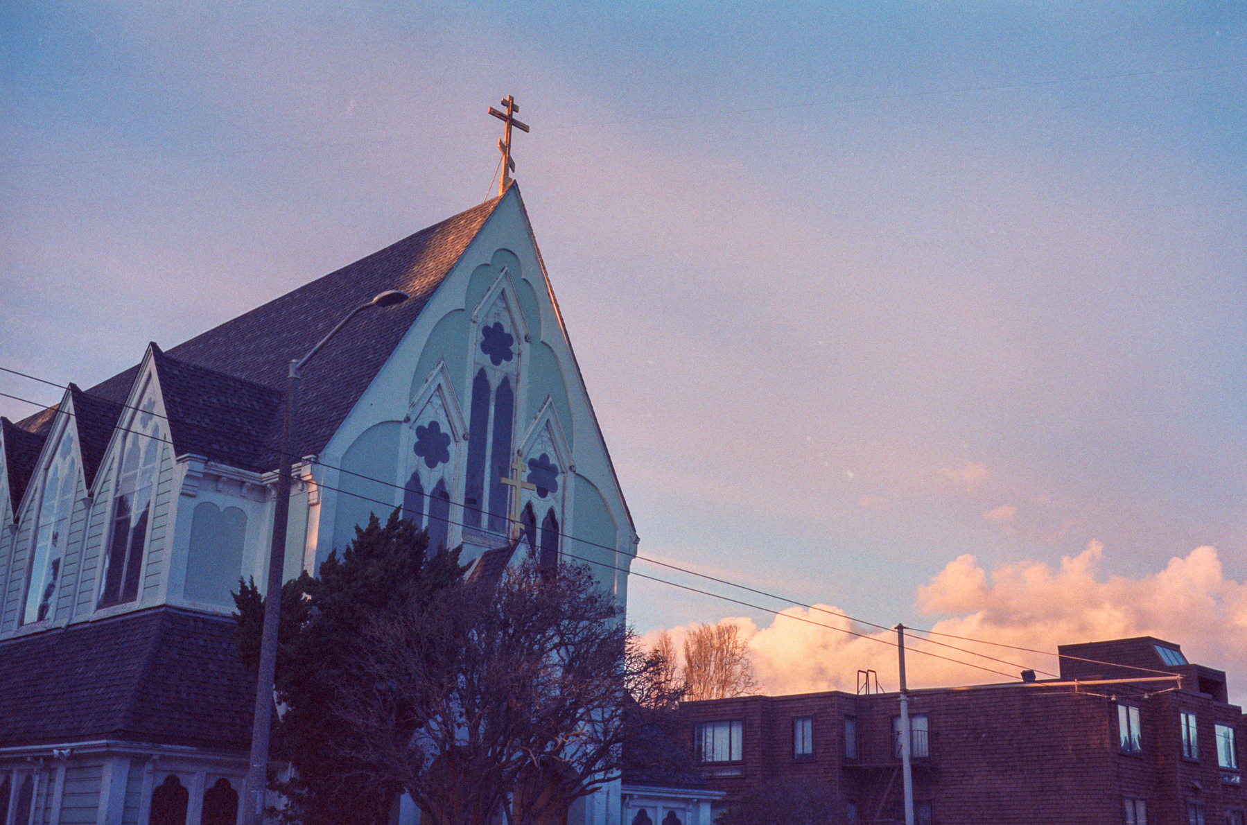 a scan of a color photograph of  a church in San Francisco that is painted blue set against a blue sky at dusk with pink hue and white clouds